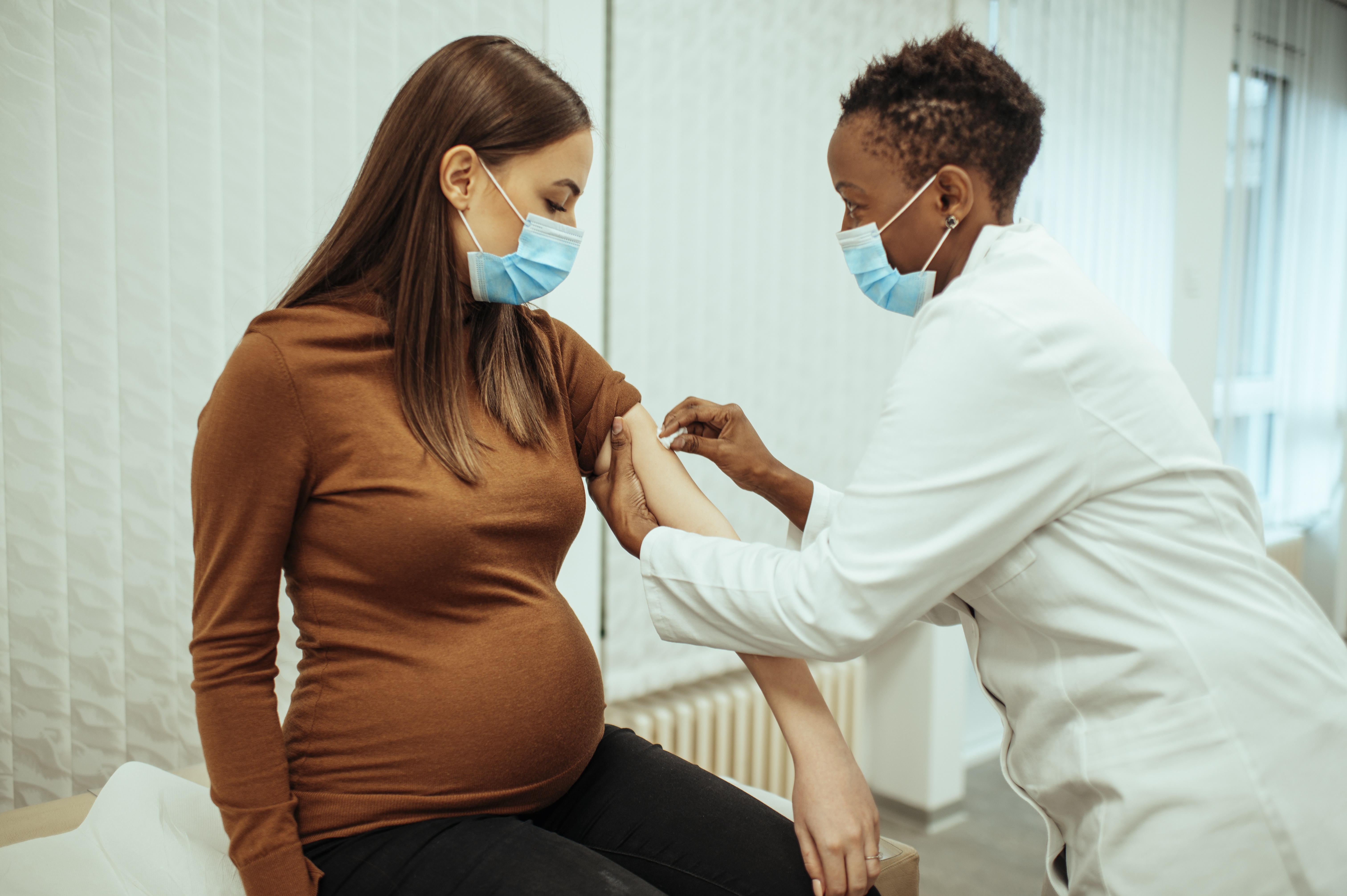 Doctora afroamericana preparando a una mujer embarazada para la vacunación. Mujer embarazada recibiendo la vacuna contra el COVID-19.