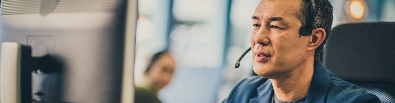 Foto de un hombre asiático adulto con auriculares utilizando una computadora mientras trabaja en un centro de llamadas.