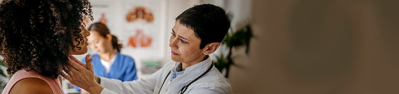 Médica que examina a una paciente en su consultorio médico mientras una profesional de enfermería escribe información de la paciente