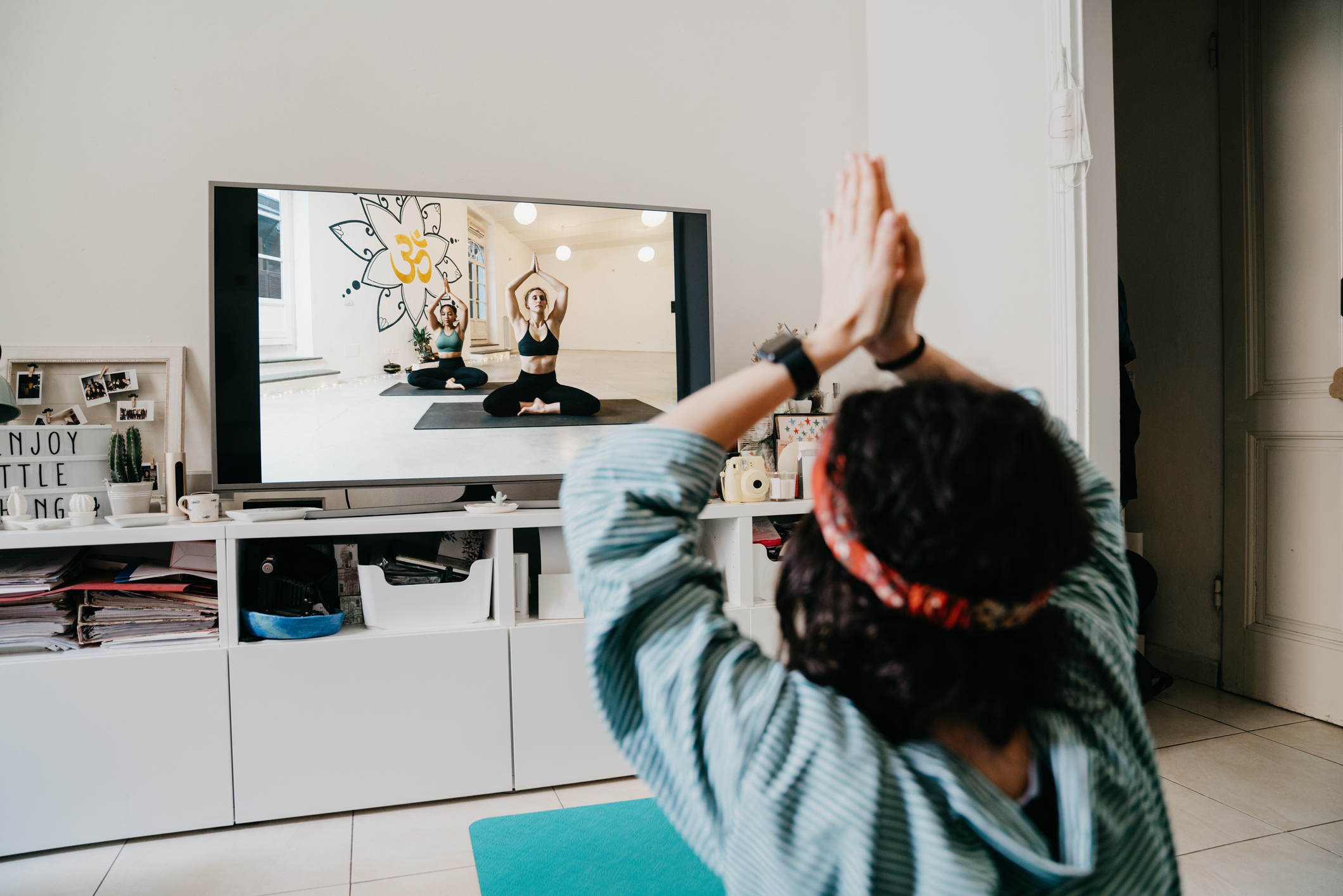 Mujer practicando yoga en el hogar con una lección en video en la televisión. Está en el hogar durante la cuarentena del coronavirus Covid-19.
