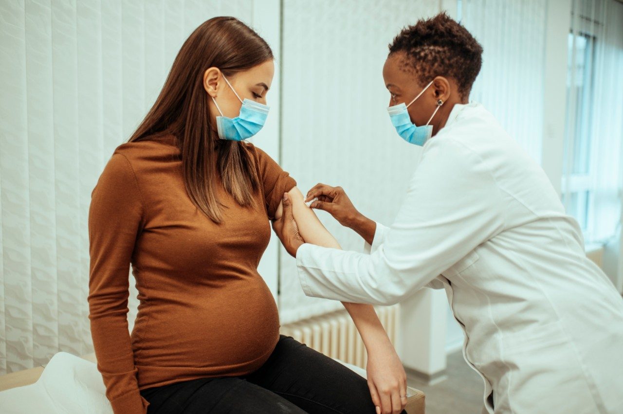 Doctora afroamericana preparando a una mujer embarazada para la vacunación. Mujer embarazada recibiendo la vacuna para la COVID-19.