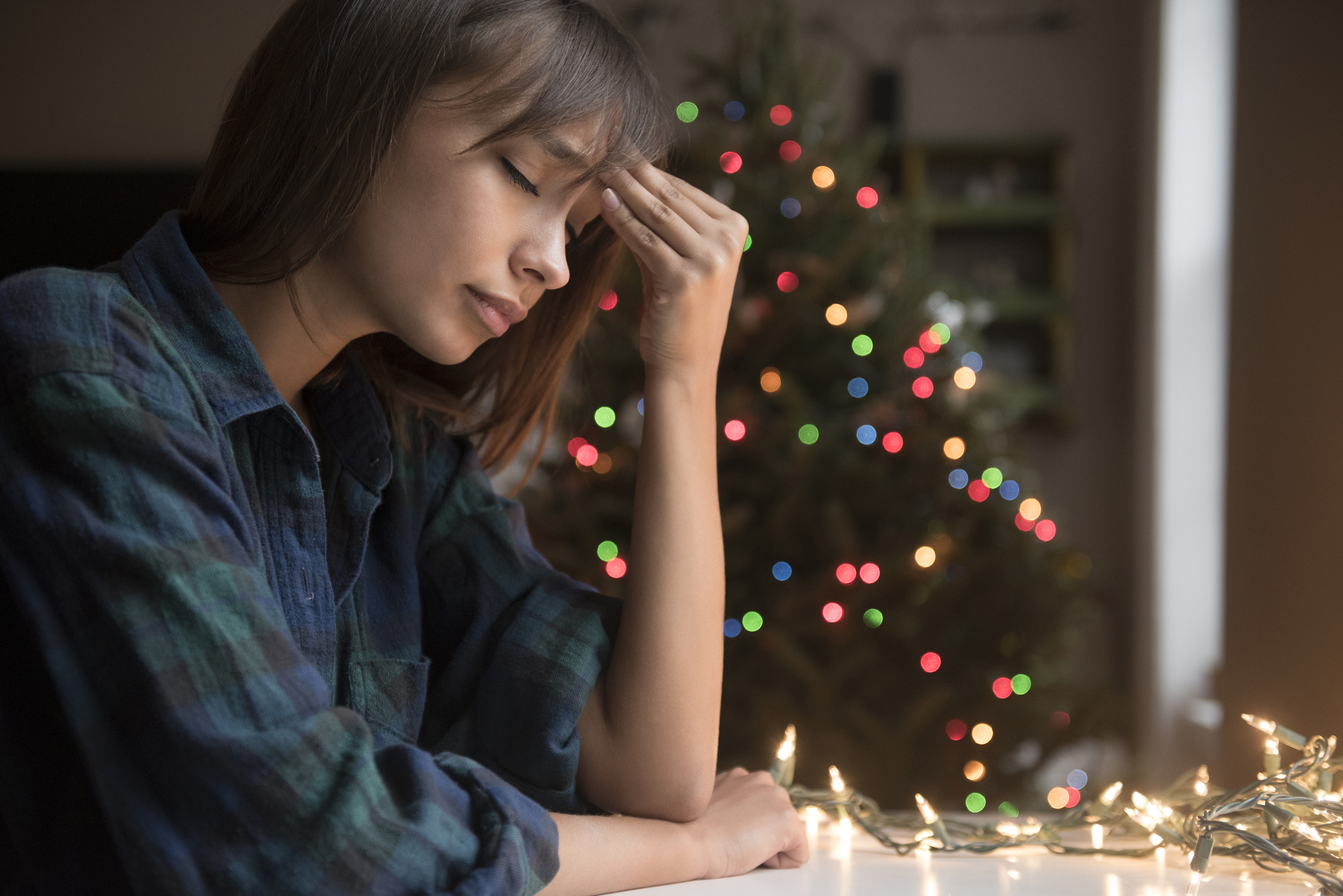 Mujer de raza mixta con dolor de cabeza cerca de un árbol de Navidad