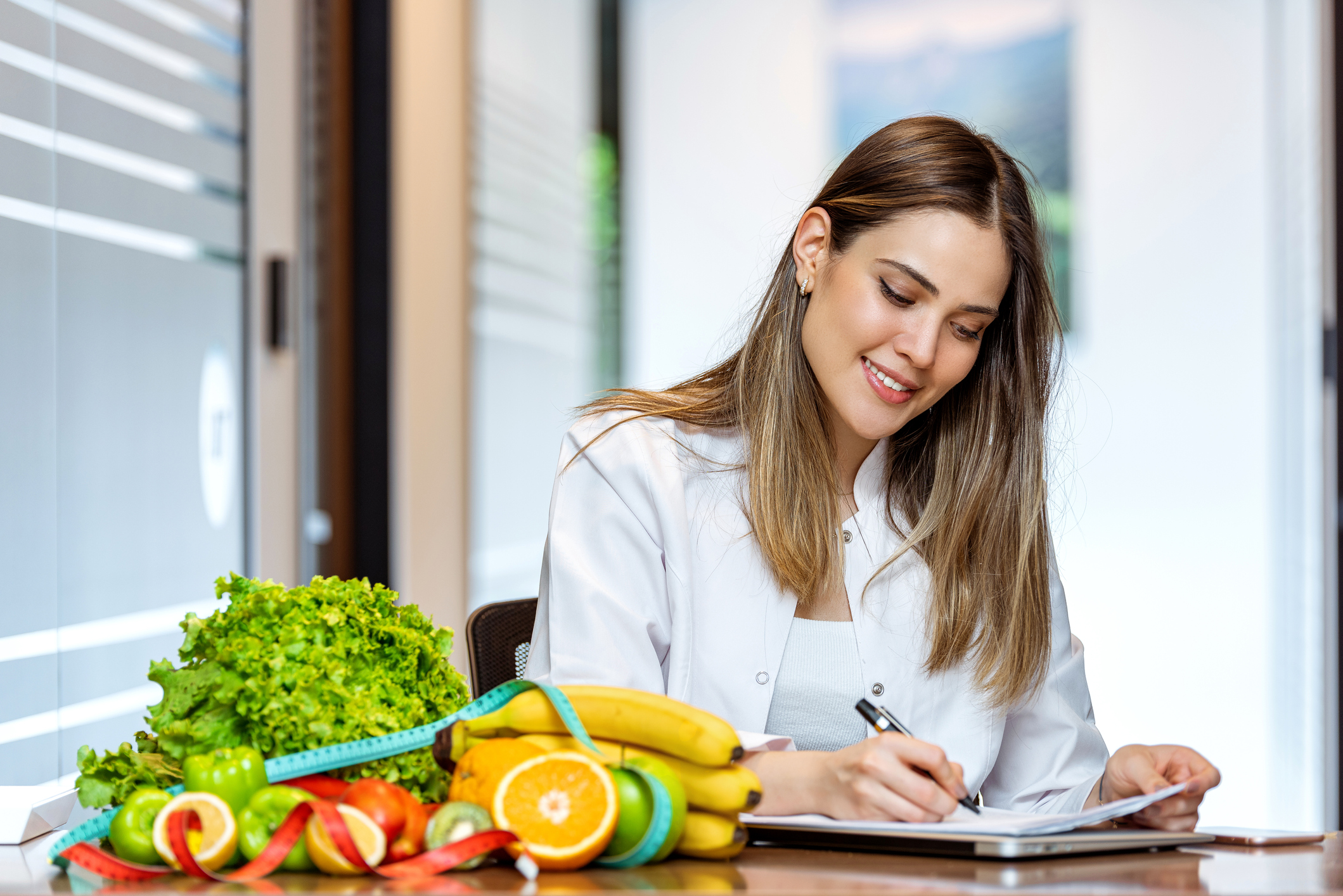 Nutricionista sonriente en su consultorio, ella muestra frutas y verduras saludables.