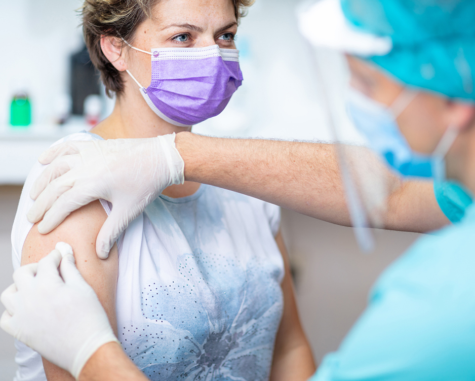 Paciente de sexo femenino con mascarilla protectora esperando la vacunación, médico usando guantes quirúrgicos desinfectando su brazo