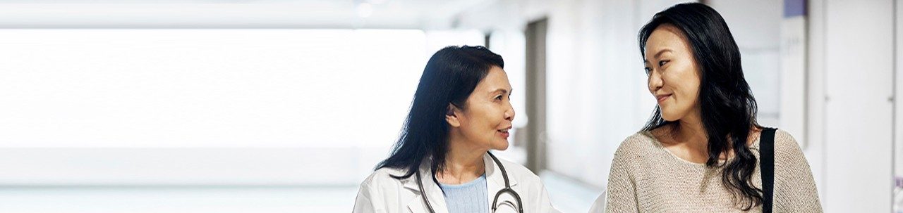 Médica madura sonriente hablando con una mujer en el hospital. Paciente de sexo femenino visitando a un trabajador de atención médica para un chequeo de rutina. Están paradas en el corredor.