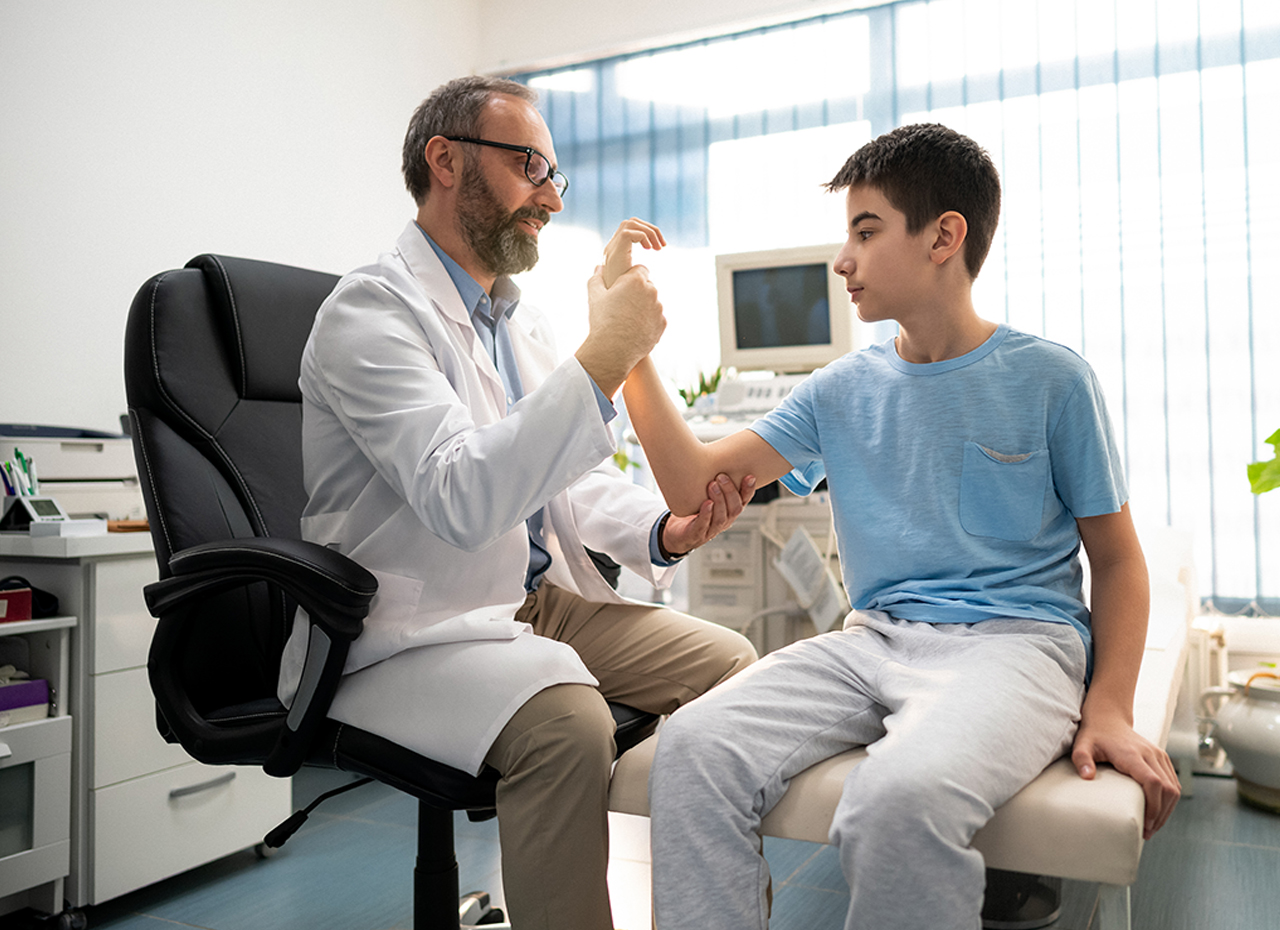 Un médico adulto examina a su paciente joven. El médico controla el estado del brazo del niño.