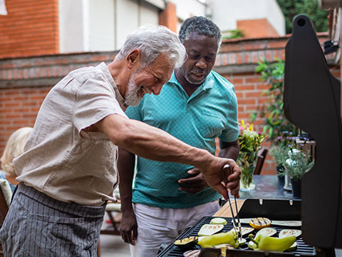 Dos adultos mayores preparando una barbacoa para una cena vegana con amigos.