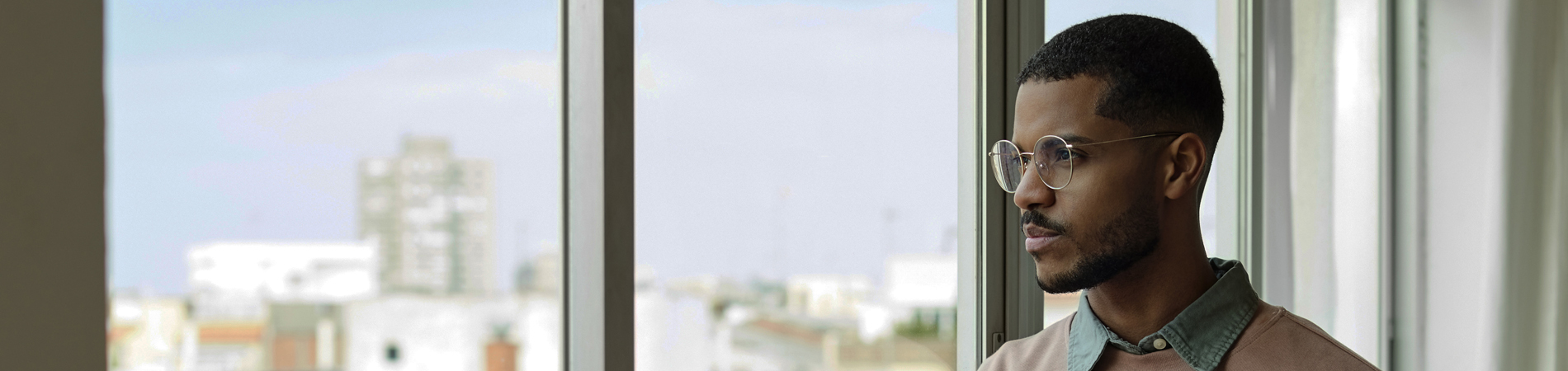 Joven guapo mirando a través de la ventana. Hombre reflexivo con un teléfono móvil en la sala de estar. Está en la oficina en casa.