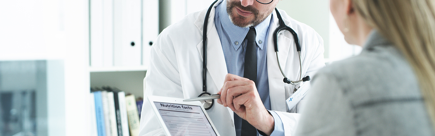 Fotografía recortada de un médico guapo de mediana edad explicando una tabla de información nutricional en una tableta digital a una paciente en su consultorio
