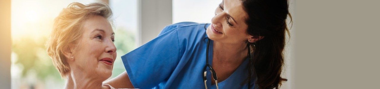 Imagen de una mujer mayor sonriente hablando con un profesional de enfermería en un centro de vida asistida