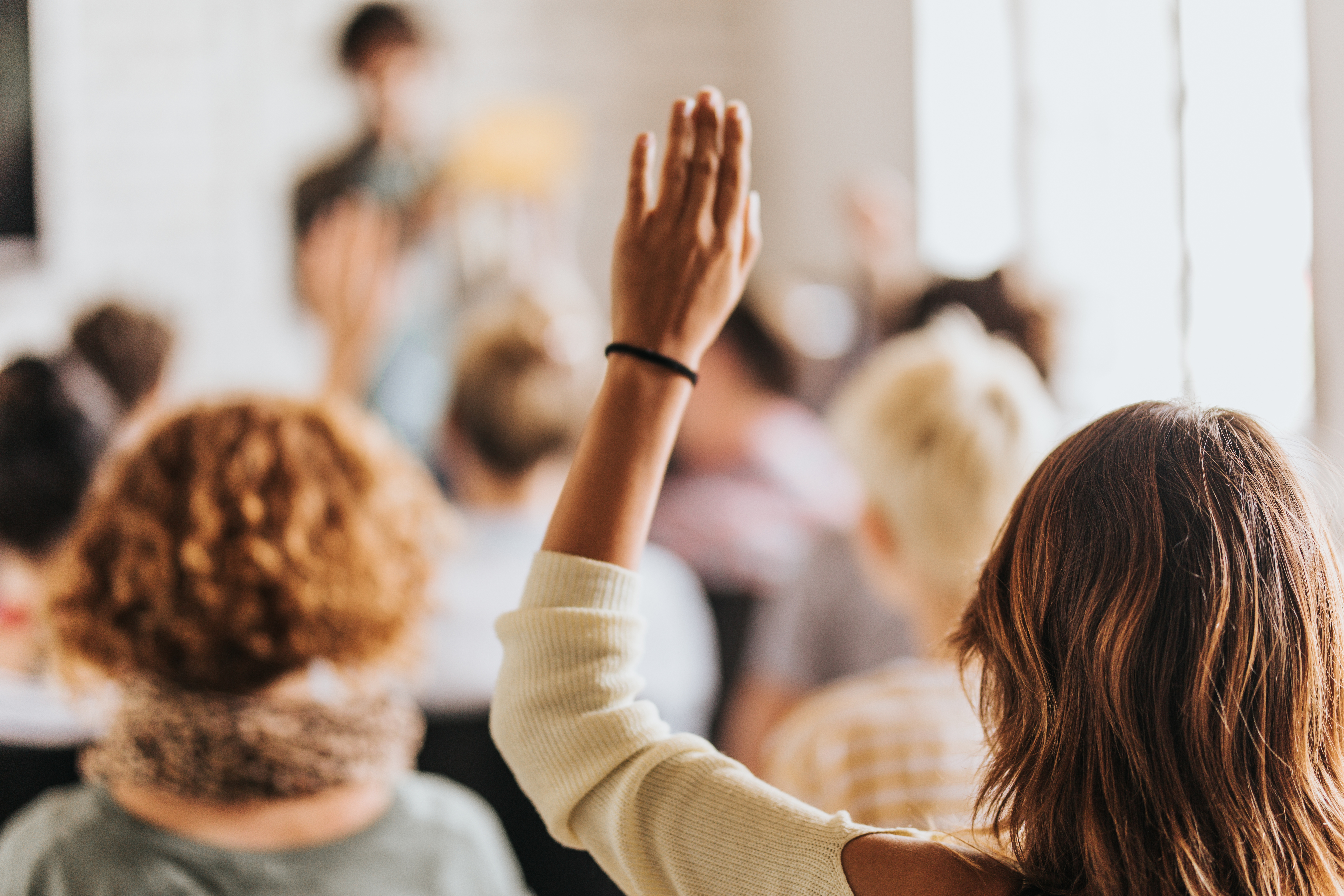 Vista trasera de una empresaria casual levantando su brazo para hacer la pregunta sobre el evento educativo en una sala de reuniones.